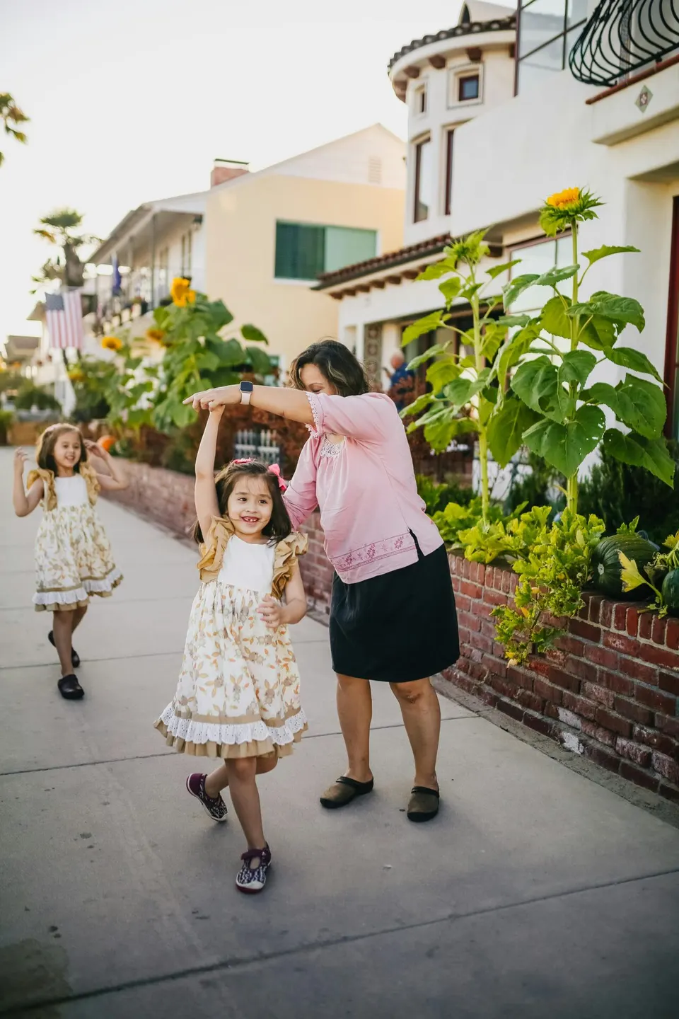 A woman dancing with two little girls on a garden sidewalk
