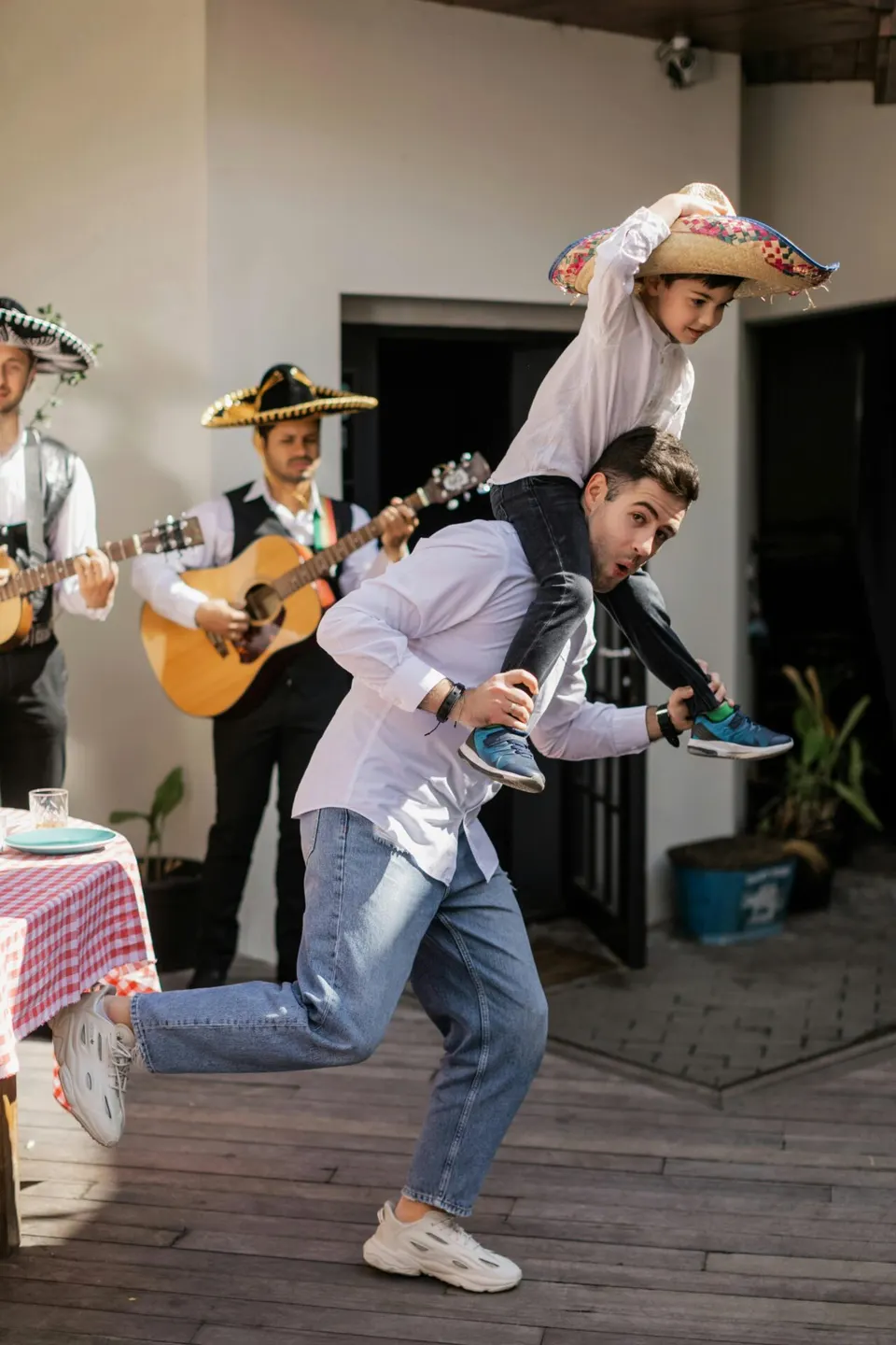 A father dancing with a child on his shoulders beside mariachi musicians