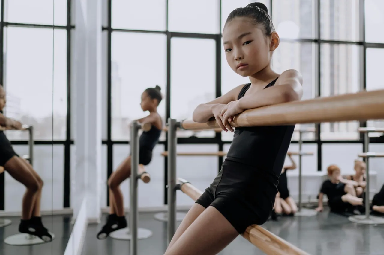 A young dancer resting at a ballet barre